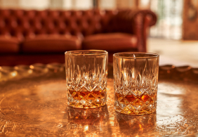 Zwei Kristallgläser mit Whisky auf einem goldenen Tablett, Hintergrund unscharf.