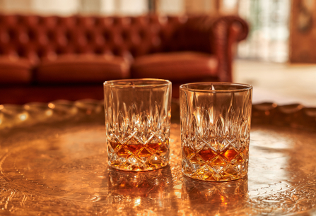 Zwei Kristallgläser mit Whisky auf einem goldenen Tablett, Hintergrund unscharf.