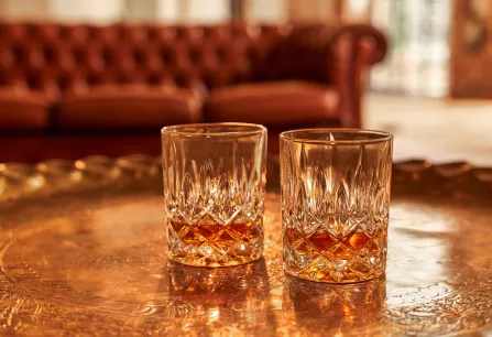 Zwei Kristallgläser mit Whisky auf einem goldenen Tablett, Hintergrund unscharf.