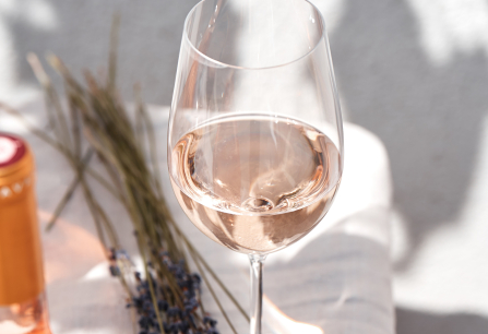 Weinglas mit Roséwein neben Lavendel auf Leinentuch.