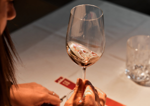 Person hält Weinglas über Tisch mit untergelegtem Papier.