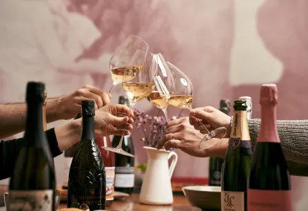 Personen stoßen mit Weißweingläsern an, umgeben von Champagnerflaschen.