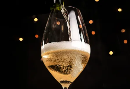 Sekt wird in ein Glas eingeschenkt, vor einem Hintergrund mit Lichtern.