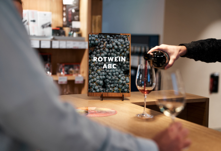 Person schenkt Rotwein in Glas, Flasche und Weingläser auf Holztheke.