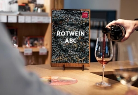 Ein Buch über Rotwein, daneben wird Rotwein in ein Glas eingeschenkt.