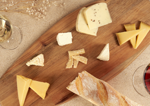 Verschiedene Käse auf Holzbrett, begleitet von Rot- und Weißwein, mit Baguette.