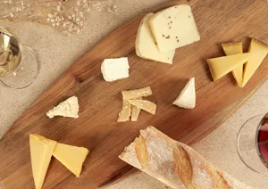 Verschiedene Käse auf Holzbrett, begleitet von Rot- und Weißwein, mit Baguette.