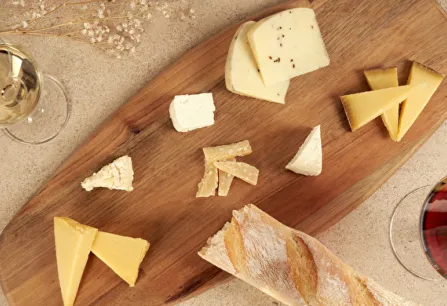 Verschiedene Käse auf Holzbrett, begleitet von Rot- und Weißwein, mit Baguette.