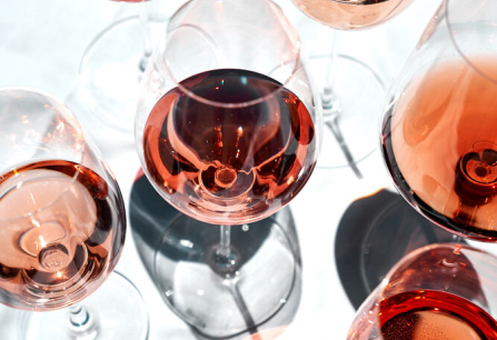 Mehrere Weingläser mit Roséwein auf weißem Hintergrund, elegante Licht- und Schatteneffekte.
