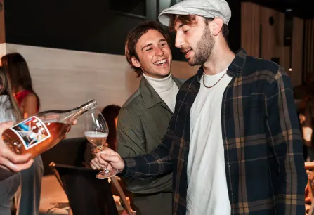 Zwei Männer lachen und stoßen mit einem Glas Roséwein an.