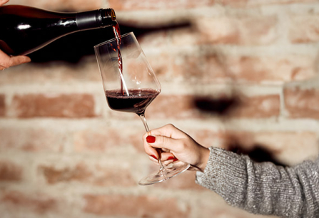 Roter Wein wird in ein stilvolles Weinglas vor einer Backsteinwand gegossen.