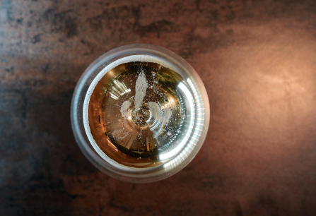 Blick von oben in ein Glas mit goldenem Getränk und Schaum auf Metalltisch.