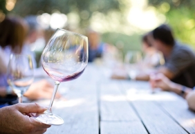 Weinglas auf Holztisch, Menschen im Hintergrund bei einem Freilufttreffen.