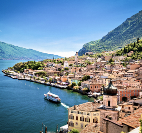 Malerische Küstenstadt mit Boot, Bergen und blauem See unter klarem Himmel.