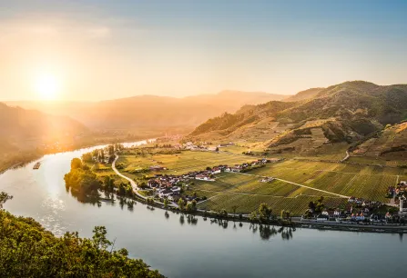 Sonnenuntergang über sanfter Flusslandschaft mit grünen Hügeln und kleinen Dörfern.