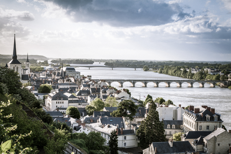 Stadtansicht mit Fluss, Brücke und Kirchturm unter bewölktem Himmel.