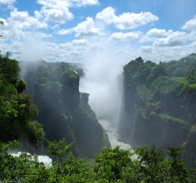 Wasserfall in grün bewachsener Landschaft unter blauem Himmel mit Wolken.