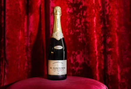 Champagnerflasche auf rosa Samthocker vor rotem Samthintergrund.