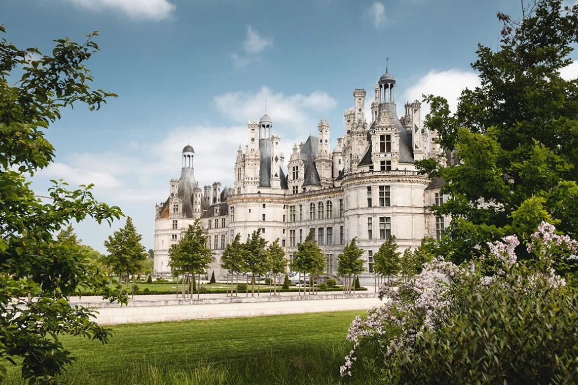 Historisches Schloss mit markanten Türmen, umgeben von gepflegtem Garten und Bäumen.