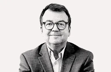 Schwarz-weiß Portrait eines Mannes mit Brille im Anzug, auf hellem Hintergrund.