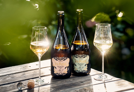 Zwei Weinflaschen und Gläser auf Holztisch unter strahlendem Sonnenlicht im Garten.