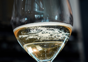 Nahaufnahme eines Champagnerglases mit sprudelndem Sekt vor unscharfem Hintergrund.