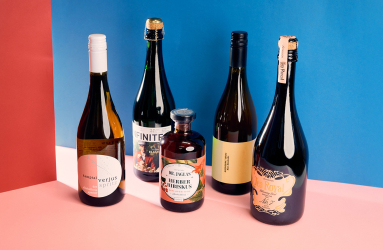 Fünf verschiedene Getränkeflaschen vor rot-blauem Hintergrund auf rosa Boden.