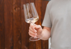 Mann hält ein gefülltes Weinglas vor Holzuntergrund.