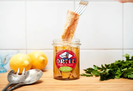 Glas mit Thunfischfilets, umgeben von Zitronen, Besteck und Kräutern.