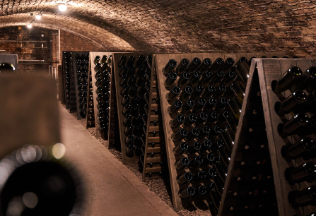 Gewölbekeller mit Holzregalen voller horizontal gelagerter Flaschen.