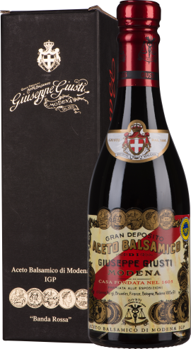 Dunkle Balsamico-Flasche mit elegantem Etikett und rotem Verschluss, neben schwarzer Geschenkbox.