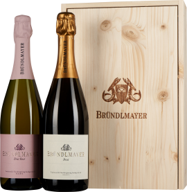 Zwei Sektflaschen mit edlen Etiketten vor einer eleganten Holzkiste.