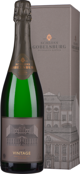 Grüne Sektflasche mit grauem Etikett und Geschenkbox im Hintergrund.