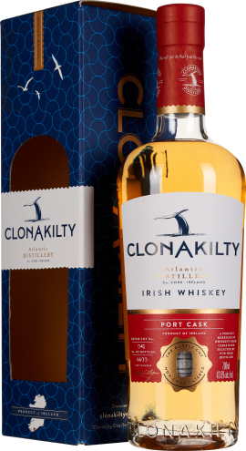 Eine elegante Flasche irischer Whiskey mit goldenem Inhalt, rotem Flaschenhals und modernem Etikettendesign vor einer stilvollen blauen Verpackung mit Wellenmuster.
