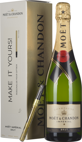 Flasche mit grünem Glas und goldfarbenem Etikett, umgeben von goldener Folie am Flaschenhals. Daneben eine elegante beigefarbene Verpackung mit schwarzem Text sowie ein goldener Stift.