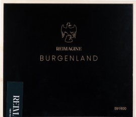 Schwarzer Kasten mit goldener Aufschrift und Adlermotiv auf Holzhintergrund.