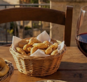 Korb mit Gebäck, Glas Rotwein und Tonkrug auf Holztisch im Freien.