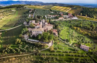 Luftaufnahme eines Dorfes mit umgebenden Weinbergen und Olivenhainen in Hügellandschaft.