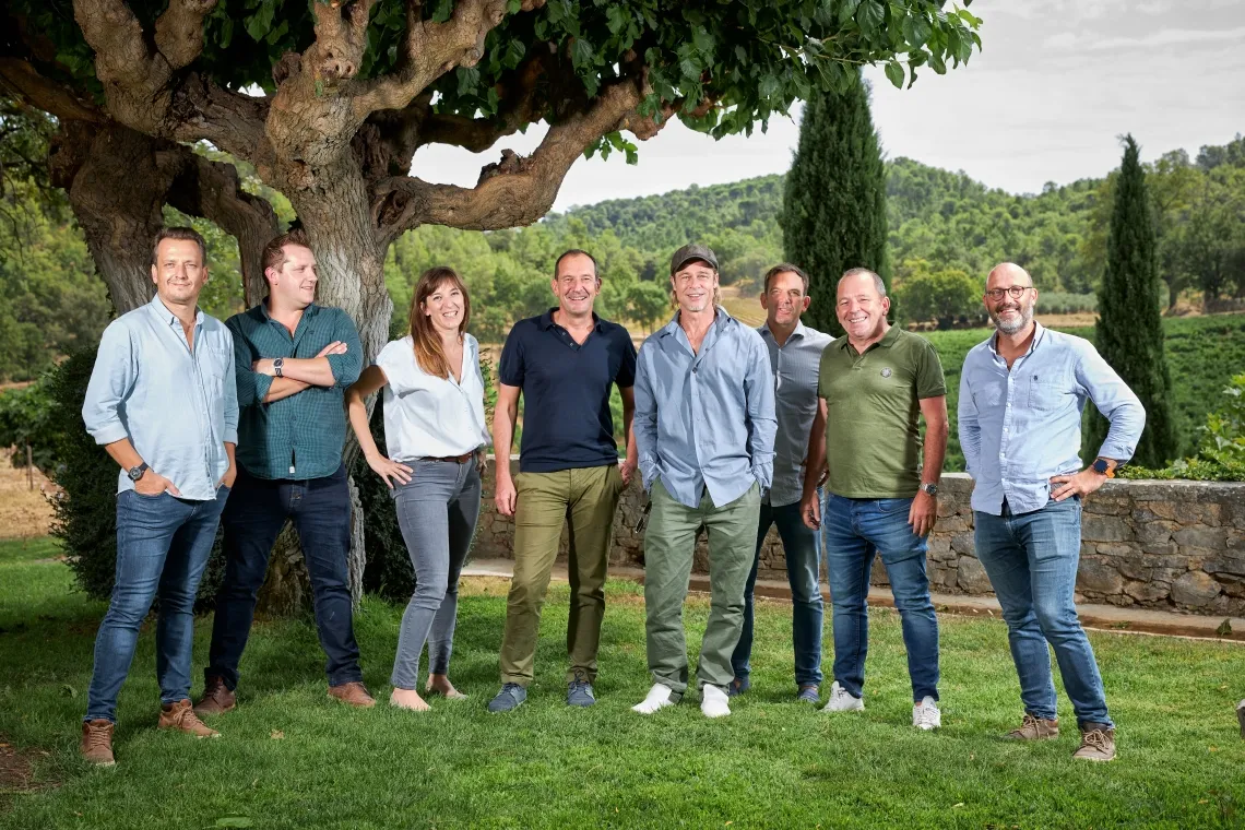 Gruppe lächelnder Menschen vor einem großen Baum in einer ländlichen Umgebung.