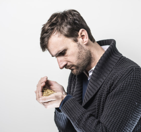 Mann in dunklem Pullover betrachtet nachdenklich eine Handvoll Getreide.