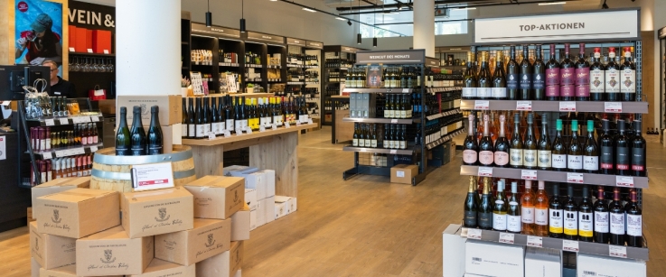 Moderner Weinladen mit Holzregalen, gefüllt mit Weinflaschen und Pappkartons.