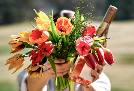 Bunter Tulpenstrauß und Roséweinflasche in Händen, mit unscharfem Naturhintergrund.