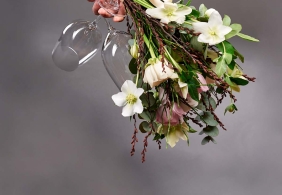 Blumenstrauß mit weißen Blüten und Weingläsern, auf grauem Hintergrund.