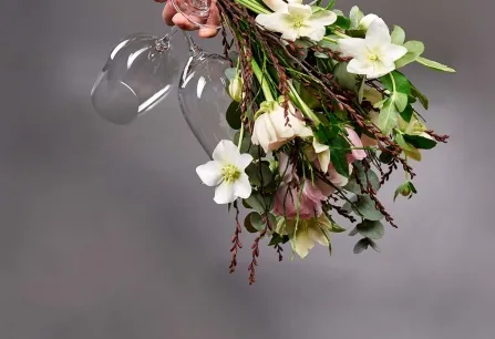 Blumenstrauß mit weißen Blüten und Weingläsern, auf grauem Hintergrund.