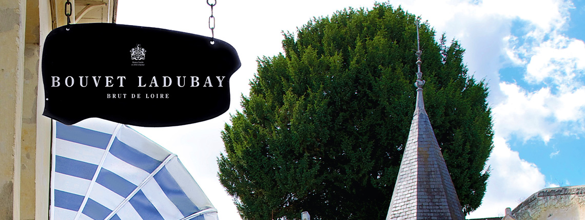 Schwarzes Ladenschild vor Baum und traditionellem Turm, blauer Himmel im Hintergrund.