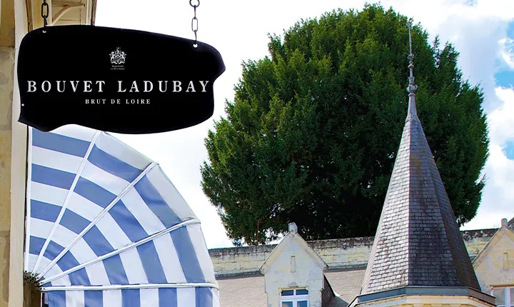 Schwarz-weiß gestreifter Sonnenschirm vor Herrenhaus mit Turm und Baum.