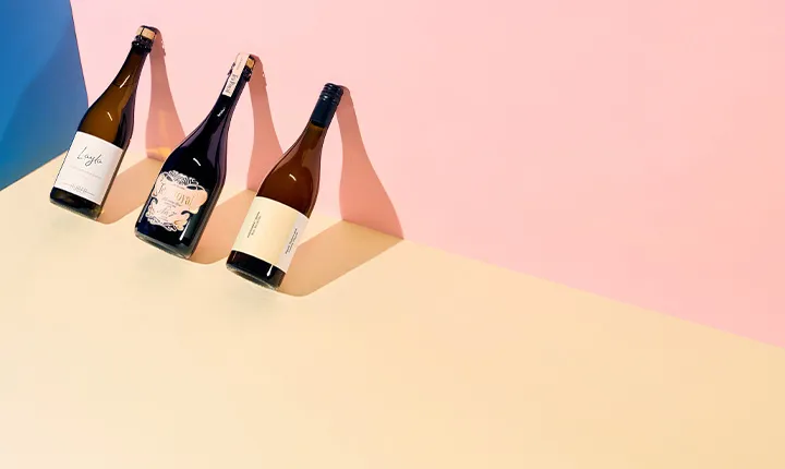 Drei Weinflaschen auf farbigem, minimalistischem Hintergrund.