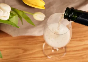 Sekt wird in ein Glas gegossen, daneben gelbe und weiße Tulpen.