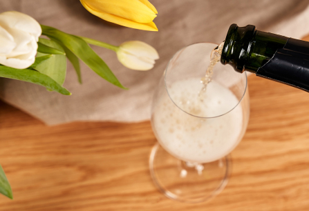 Sekt wird in ein Glas gegossen, daneben gelbe und weiße Tulpen.